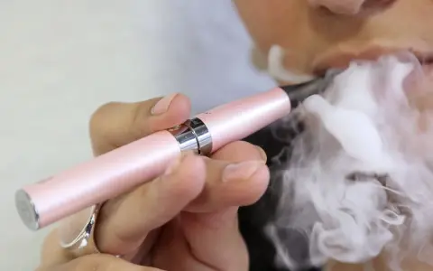 Persona exhala vapor de un cigarrillo electrónico rosa. ¿Qué es peor el vaper o el tabaco?