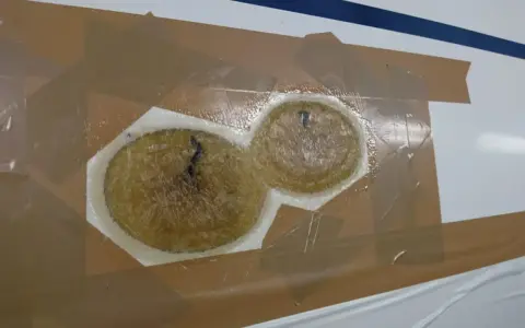 Reparaturstelle an einem Boot, bereit für das gelcoat erneuern. Zwei runde, faserige Füllungen sind mit Klebeband abgedeckt.