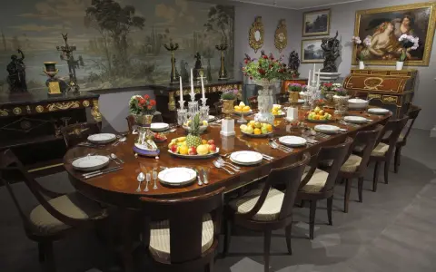 Table dressée dans un style directoire, avec fruits, fleurs et vaisselle raffinée. Le décor mural évoque un paysage champêtre.