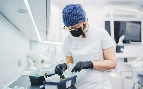 Dentystka w czepku i masce przygotowuje materiały, w tym te do zabiegów z użyciem abrazji powietrznej.