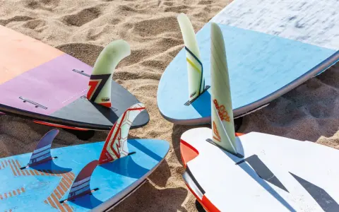 Mehrere Windsurfboards mit bunten Finnen liegen im Sand. Perfekt, wenn Sie ein Windsurfboard kaufen möchten.