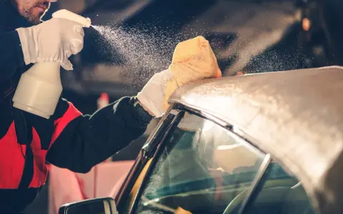 A person in gloves sprays a convertible car's fabric top with cleaning solution, then wipes it with a sponge. This is how you wash a convertible car.