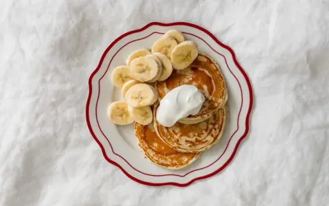 Placuszki bananowe dla niemowlaka na talerzyku z kremem i plasterkami banana.