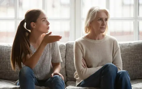Junge Frau gestikuliert wütend, während ihre Mutter abgewandt sitzt. Es scheint, als ob meine Tochter mich hasst.