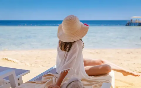 Dziewczynka w kapeluszu na plaży, marząca o tym, gdzie warto polecieć. Piękne morze i słońce zachęcają do odpoczynku.
