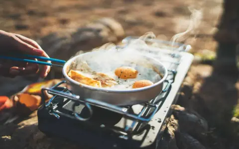 Spiegeleier und Brot brutzeln in einer Pfanne auf einem Gaskocher. Perfekte Camping Rezepte für unterwegs.