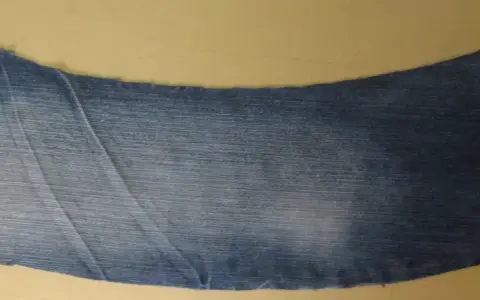 Ett utskuret jeansstycke med en vågig kant, redo att sys till en volang. Röd tråd syns längs ena sidan.