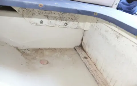Le fond de cale d'un bateau, sale et moisi, avec des traces d'humidité et de débris.