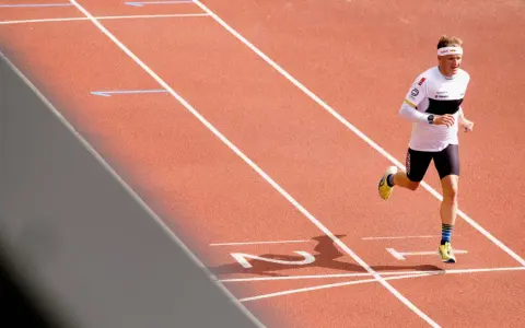 Läufer mit Stirnband und Laufbekleidung auf einer roten Laufbahn, der sich auf sein polarisiertes Training konzentriert.