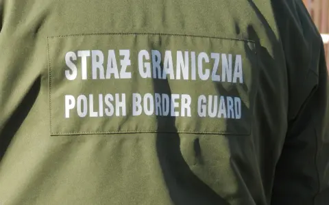 Fragment zielonego munduru Straży Granicznej z białym napisem "STRAŻ GRANICZNA POLISH BORDER GUARD".