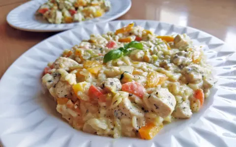 Szybkie risotto z warzywami i kurczakiem, udekorowane listkiem bazylii. Pyszne i kolorowe danie na talerzu.