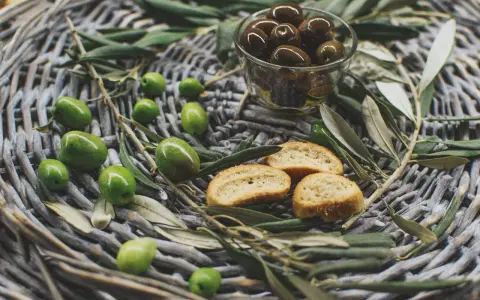 Olives vertes et noires, crostinis et feuilles d'olivier sur un panier tressé, évoquant une spécialité culinaire du Luberon.