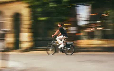 Mężczyzna na rowerze typu s-pedelec pędzi ulicą, rozmyte tło sugeruje dużą prędkość.
