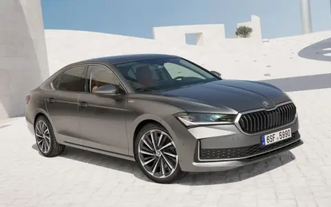 Szary sedan Skoda Superb, segment d, zaparkowany na tle nowoczesnej architektury.