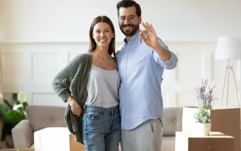 Couple heureux tenant les clés de leur nouvelle maison. L'homme fait le signe OK, symbolisant la réussite de leur projet immobilier, sans annulation offre d'achat par l'acheteur.