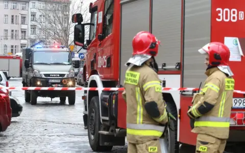 Dwóch strażaków w hełmach i mundurach stoi przy wozie strażackim. W tle wóz saperski. Starszy ogniomistrz zarobki to marzenie wielu, ale oni służą.