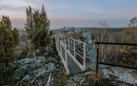 Mostek na skalnym ostańcu na Jurze Krakowskiej. W oddali las i niebo o zmierzchu.