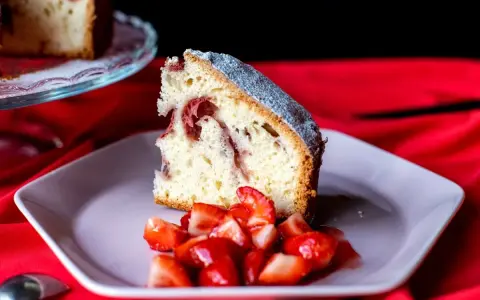 Un trozo de bizcocho de fresa esponjoso, espolvoreado con azúcar glas, servido con fresas frescas cortadas en un plato rosa.
