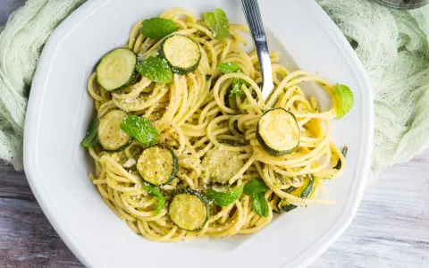 Spaghetti con zucchine cremosa, guarniti con foglie di menta fresca e parmigiano grattugiato. Un piatto leggero e gustoso.