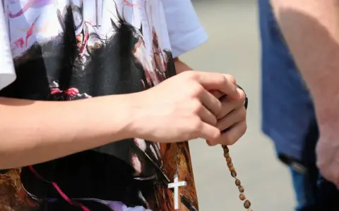 Dłoń trzyma paciorki różańca, a na koszulce widnieje biały krzyż. To znak modlitwy, żeby się wszystko ułożyło.