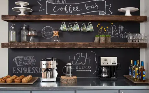 Un angolo caffè fai da te con macchine, tazze, muffin e scritte alla lavagna.