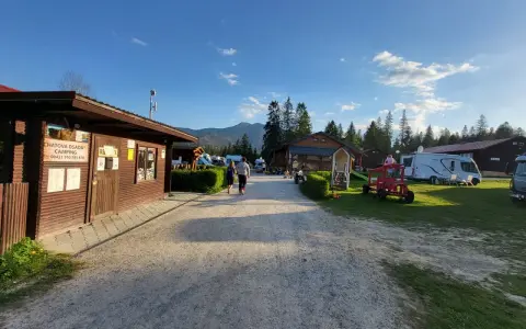 Słoneczny dzień na **camping Oravice**. Drewniany budynek recepcji, przyczepy kempingowe i zielone wzgórza w tle.