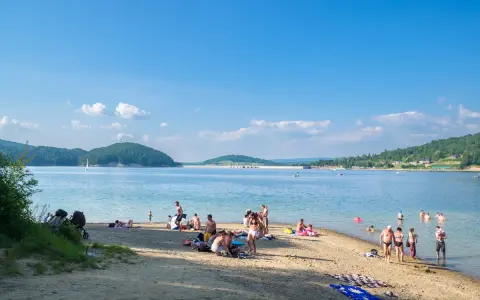 Polańczyk atrakcje: plażowicze odpoczywają nad Soliną, w tle żaglówka i zielone wzgórza.