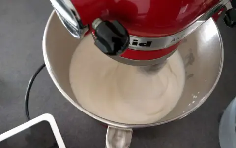 Un robot pâtissier rouge mélange une crème onctueuse, étape clé pour réussir une pâte à bombe aérienne.
