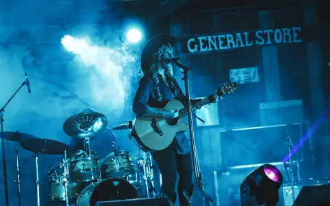 Artystka w kapeluszu gra na gitarze, wykonując najpopularniejsze piosenki country. W tle perkusja i napis "GENERAL STORE".