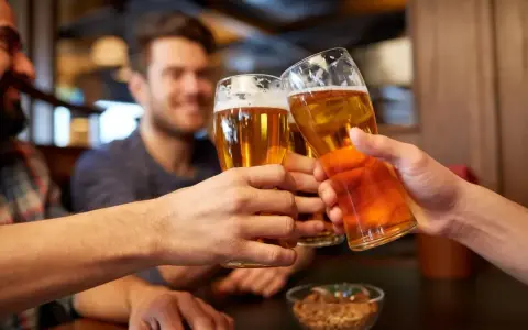 Trzech przyjaciół wznosi toast piwem. Widać ich dłonie trzymające szklanki z bursztynowym napojem, a na stole miseczkę z orzeszkami. To idealny moment, by porozmawiać o zawartości alkoholu w piwie.