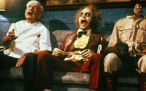 Tre personaggi bizzarri, tra cui Beetlejuice, siedono su un divano in una scena di horror comedy.