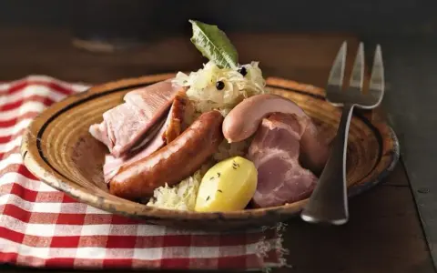 Assiette de choucroute garnie, évoquant son origine alsacienne, avec saucisses, lard, jambon et pommes de terre.