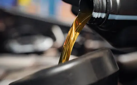 Goldfarbenes Motoröl fließt aus einem schwarzen Behälter in einen dunklen Trichter.
