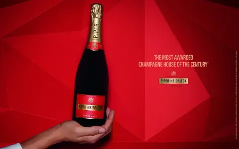 Eine Hand hält eine Flasche Piper-Heidsieck Champagner vor rotem, geometrischem Hintergrund.