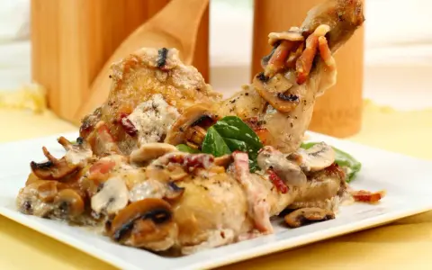 Delicioso pollo con champiñones y tocino en una cremosa salsa, servido en un plato blanco.