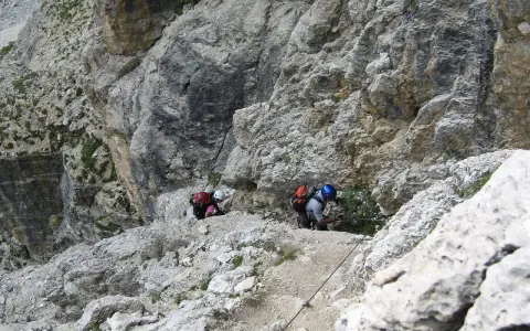 Dwóch turystów pokonuje via ferraty w Dolomitach, wspierając się na stalowej linie.