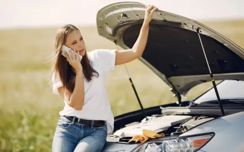 Mujer llama por teléfono con el capó abierto, preocupada por qué pasa si el coche se queda sin aceite.