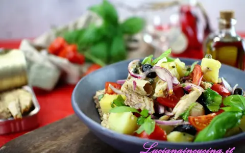 Un'insalata pantesca colorata con patate, pomodorini, olive, cipolla rossa e pesce, guarnita con basilico fresco.