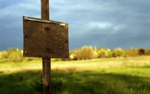 Drewniany znak na polu, jak sprawdzić granice działki? Tło z chmurami i drzewami.