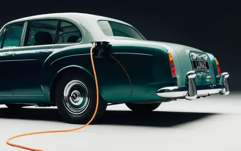 Clásico Bentley con cable de carga naranja conectado. Un ejemplo de retrofit que es la electrificación de vehículos antiguos.