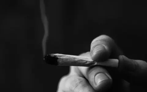 A hand holds a lit joint, smoke curling upwards. This image prompts reflection on whether Christians can smoke weed.