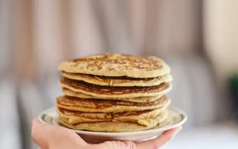 Pile de pancakes dorés à la farine de sarrasin, servis sur une assiette blanche tenue par une main.