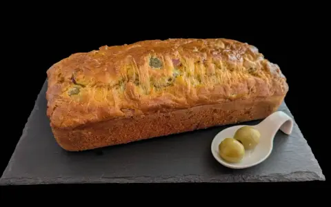 Un délicieux cake jambon olive, doré et moelleux, servi avec deux olives vertes sur une cuillère.