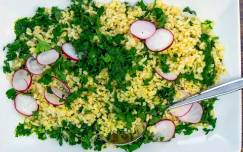 En fräsch bulgursallad med rädisor och färska örter, serverad på en vit tallrik med en sked.