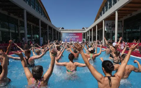 Folla entusiasta partecipa a una lezione di acquagym all'aperto, con le braccia alzate, durante la fiera dello sport Rimini.