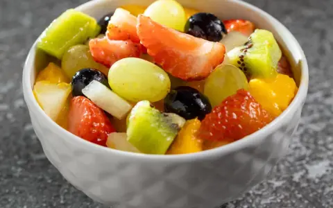 Kolorowa sałatka na imprezę: truskawki, kiwi, winogrona, mango i czarne porzeczki w białej miseczce.