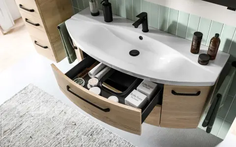Aménagement salle de bain moderne avec lavabo blanc, robinetterie noire et tiroirs en bois clair organisés.