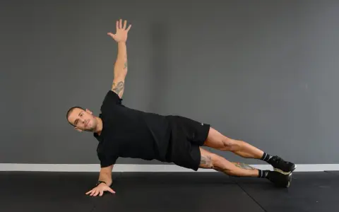 Uomo in posizione di side plank, con un braccio sollevato e l'altro appoggiato a terra.
