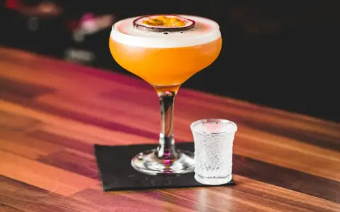 Pomarańczowy koktajl Pornstar Martini z owocem marakui, obok kieliszek z bąbelkami. Zastanawiasz się nad jego kcal?
