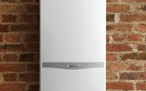 Caldaia Vaillant bianca, con logo, montata su parete in mattoni. Le dimensioni della caldaia sono compatte per adattarsi a spazi ridotti.